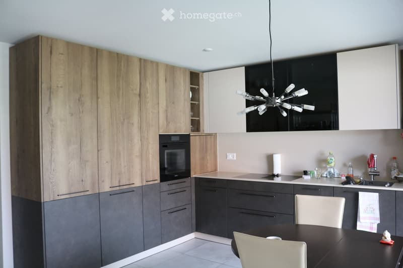 Modern kitchen with wooden and grey cabinets, a central island, a hanging light fixture, and a dining area with a table and chairs.