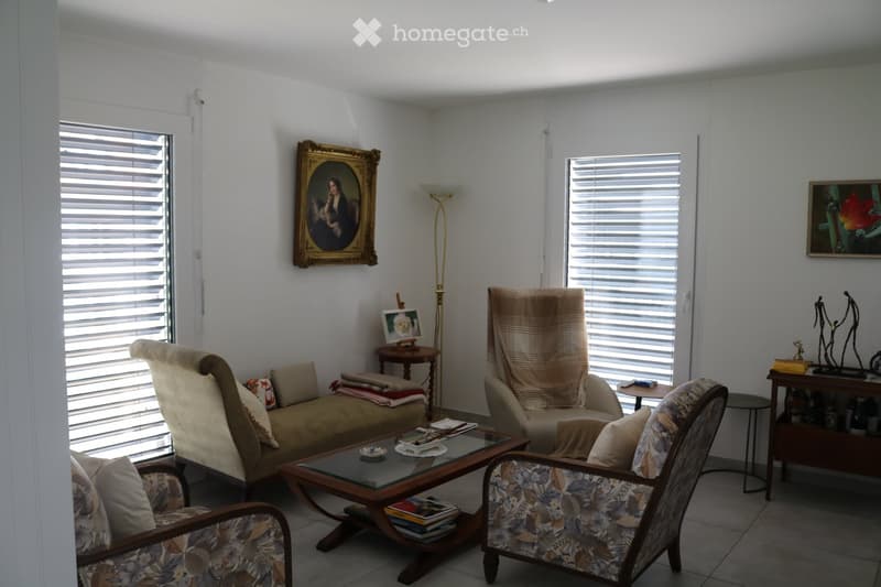 Living room with a sofa, two armchairs, a coffee table, a floor lamp, and decorative items including picture frames and a shelf.