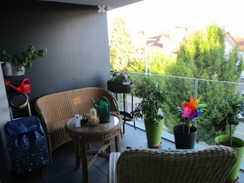 Balcony with wicker furniture, small table, potted plants, and decorative items.