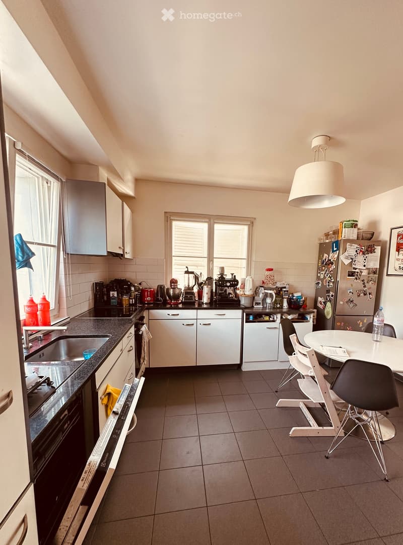 Modern kitchen with white cabinets, black countertops, stainless steel appliances, and a dining area with a round table and chairs.