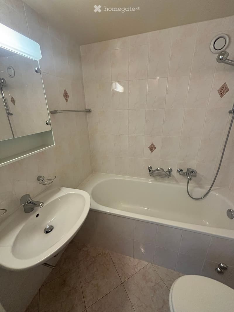 Bathroom with a bathtub, sink, mirror, and toilet. Light-colored tiles and modern fixtures.