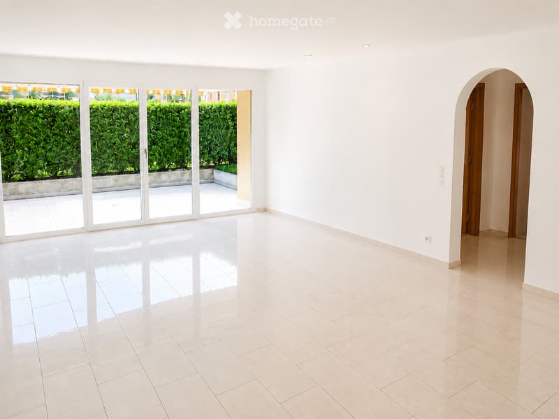 Empty room with white walls, tiled floors, large sliding glass doors leading to a patio, and an arched doorway.