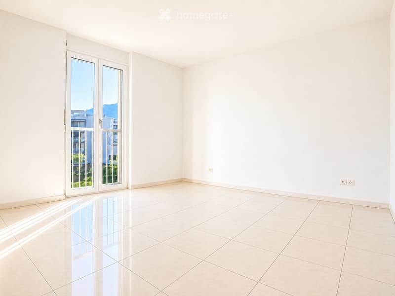 Empty room with white walls, tiled floor, and large sliding glass doors leading to a balcony with a view of the mountains and buildings.