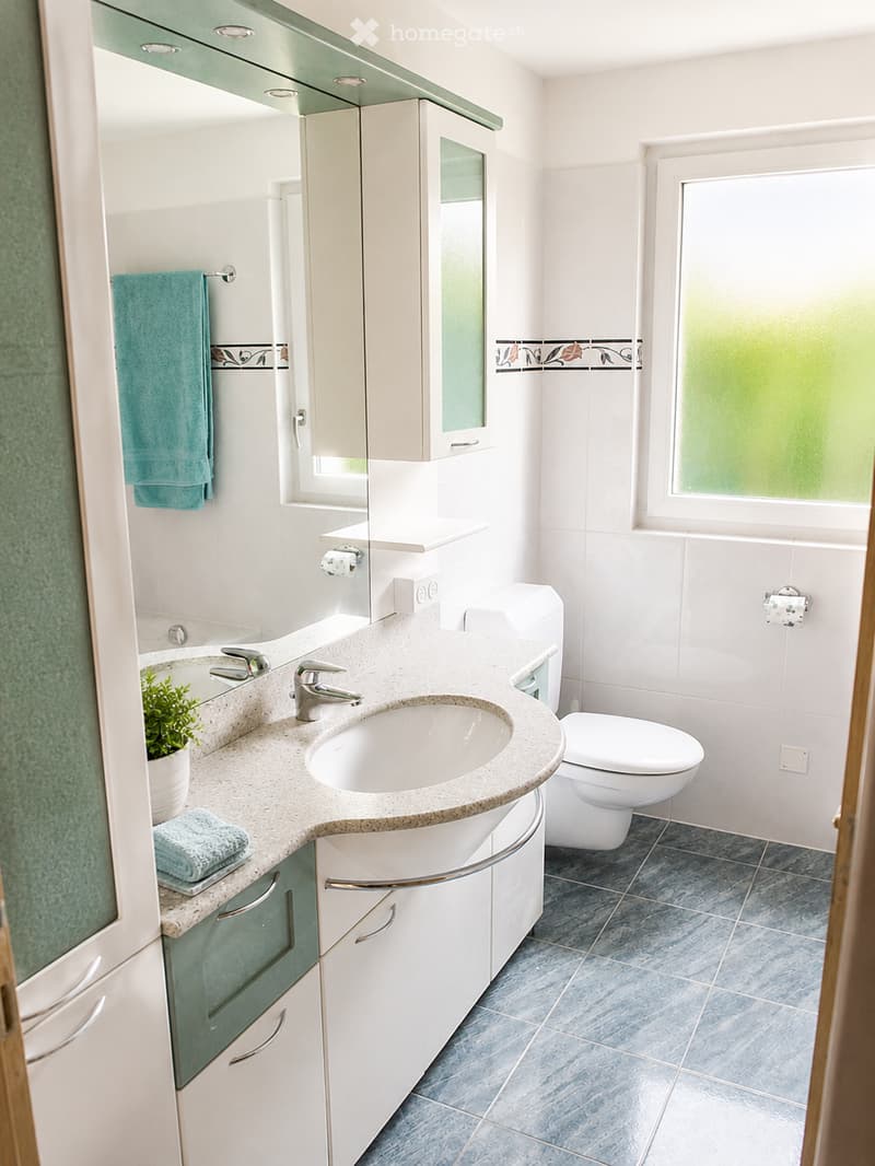 Modern bathroom with a white sink, chrome faucet, toilet, mirrored cabinet, and decorative towels.