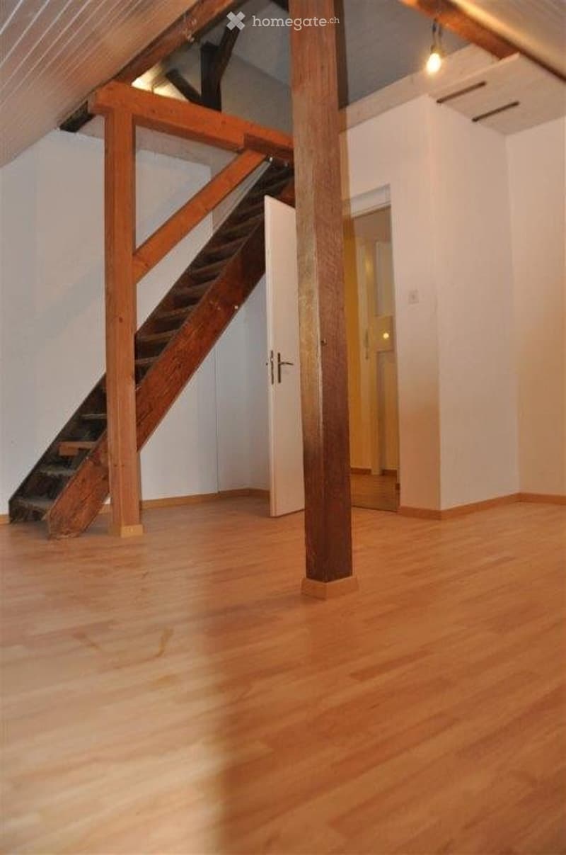Empty room with wooden flooring, white walls, and a wooden staircase leading to another level. No furniture or equipment present.