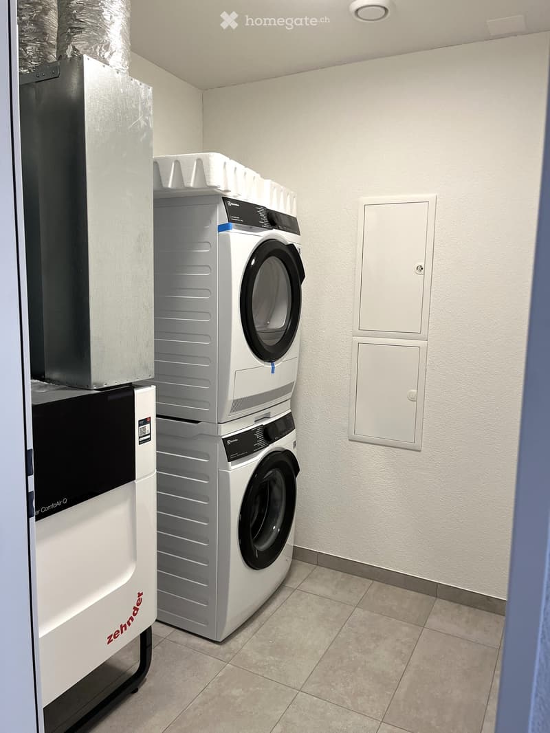 Clean, modern laundry area with a stacked washer and dryer unit, white walls, and tiled floor.