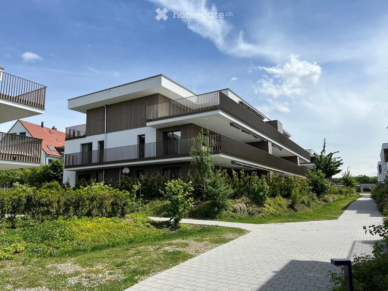 Modern two-story building with balconies, surrounded by greenery and a paved pathway.