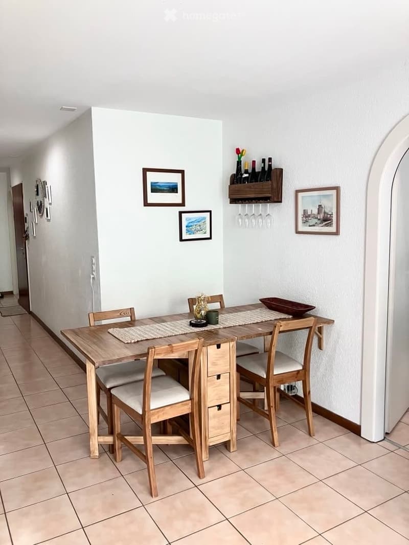 A modern dining area with a wooden dining table and four matching chairs, a wine rack with bottles and glasses, and decorative picture frames on the wall.