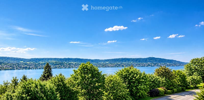 Scenic view of a lake surrounded by lush green trees and hills under a clear blue sky.