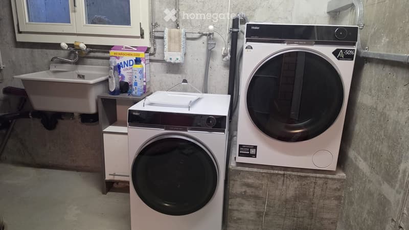 Bathroom with a sink, washing machine, and dryer. Cleaning supplies and a towel are visible on the sink counter.