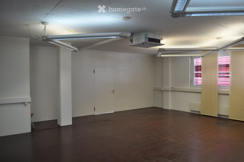 Empty room with white walls, brown tiled floor, white door, window with red blinds, ceiling with hanging lamps and air conditioning unit