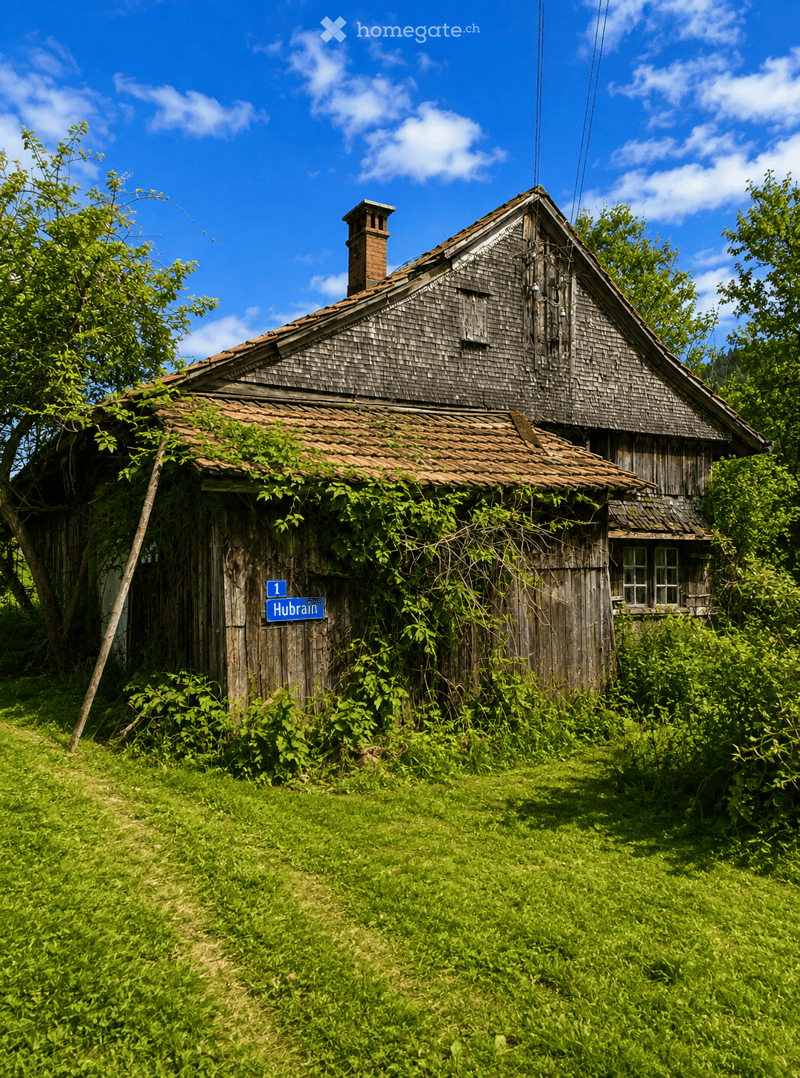 A rustic wooden house with a tiled roof and chimney, surrounded by overgrown vegetation and trees. The house has a weathered appearance with visible wooden planks and a small window.