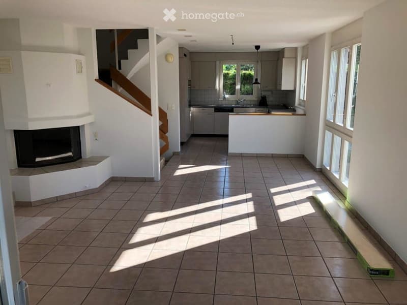 Open-plan living and dining area with a fireplace, staircase leading to an upper level, and an adjacent kitchen area with cabinets, sink, and faucet.