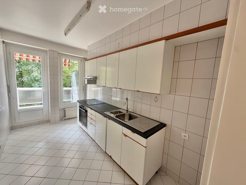 Modern kitchen with white tiled walls, white cabinets, black countertop, stainless steel sink, and built-in oven.
