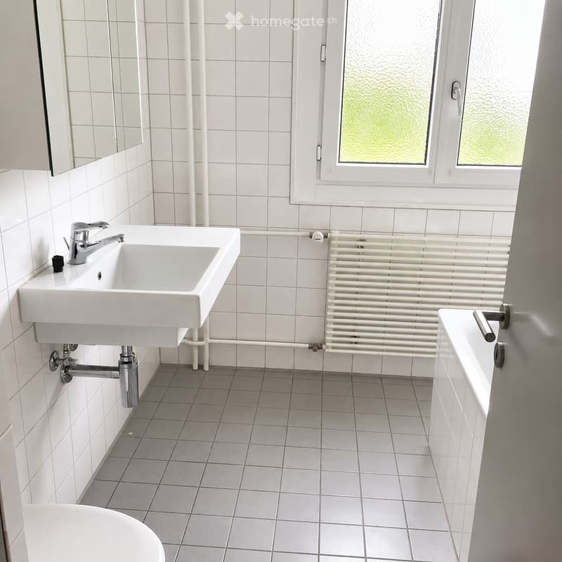 Modern bathroom with white tiles, a sink with a chrome faucet, a bathtub, a radiator, and a mirror.