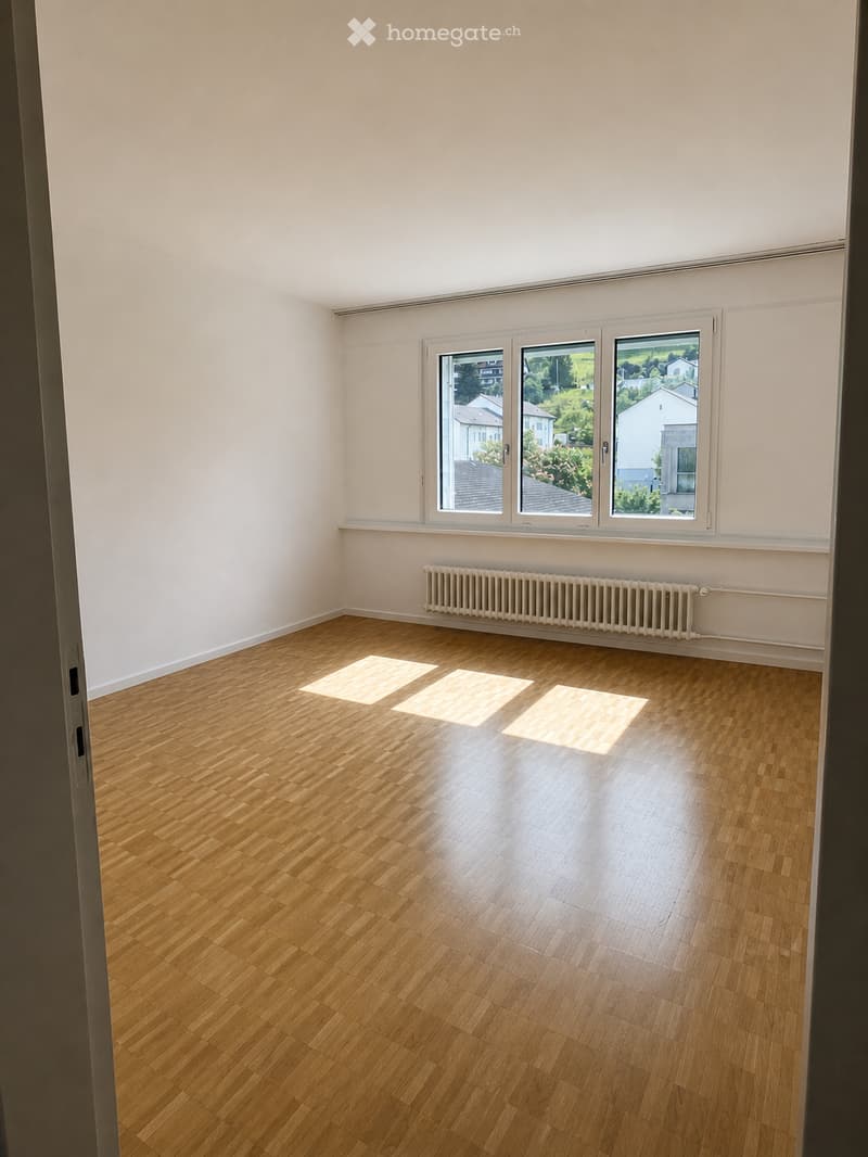 Empty room with wooden flooring, white walls, large windows, and a radiator. No furniture or equipment present.