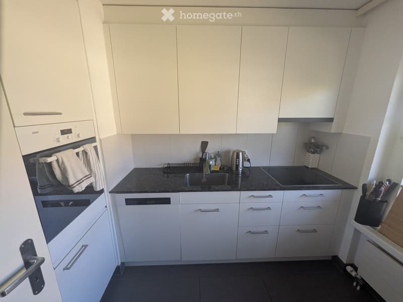 Modern kitchen with white cabinets, black countertops, stainless steel appliances, and a sink with a faucet.