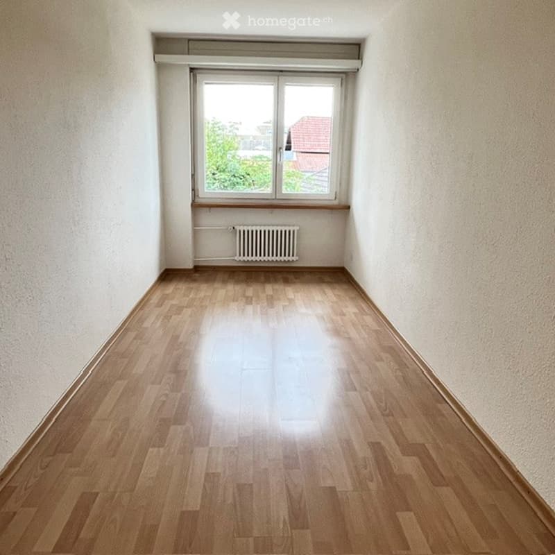 Empty room with wooden flooring, white walls, and a single window with a radiator below it.
