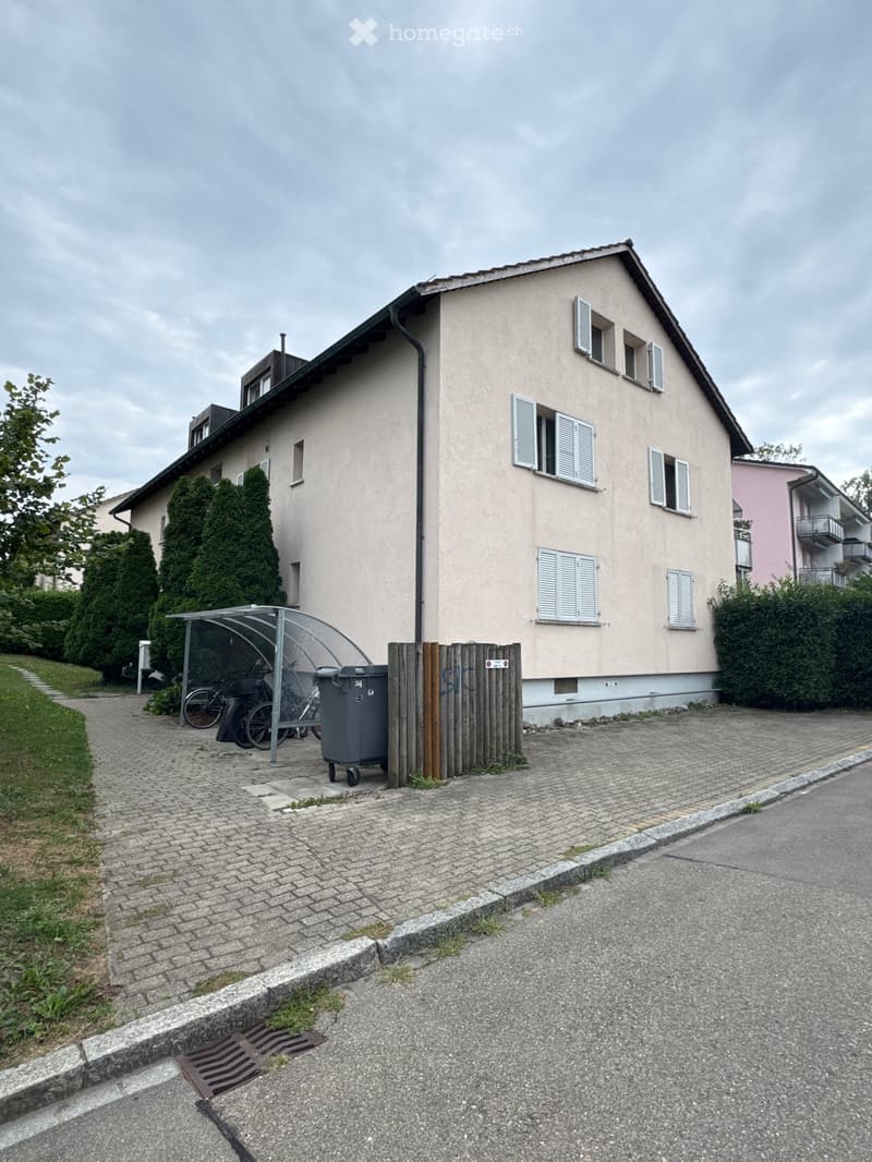 Two-story house with beige facade, white shutters, and a covered bicycle parking area.