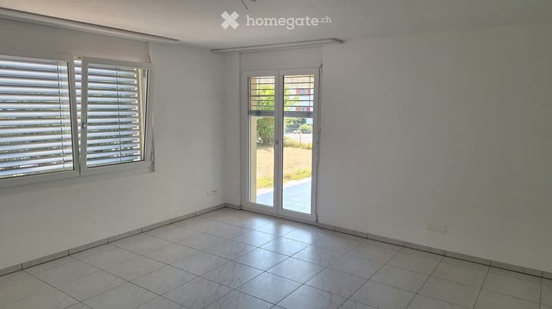 Empty room with tiled floor, white walls, large window with blinds, and sliding glass door leading to outdoor area.