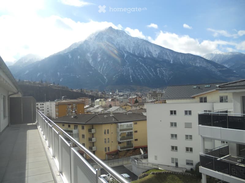 Balcony overlooking a town with buildings and snow-capped mountains in the background.