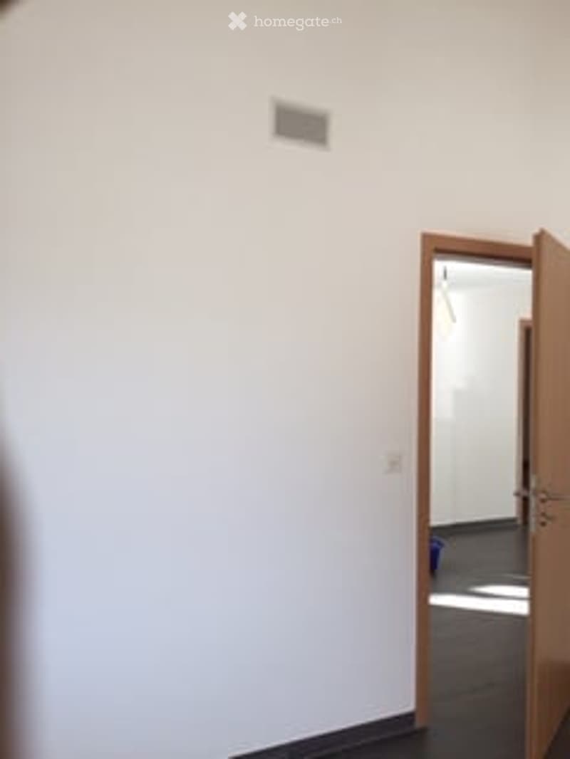 Empty room with white walls, dark flooring, and an open doorway leading to another room.