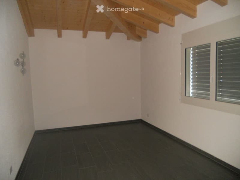 Empty room with exposed wooden beams on the ceiling, dark tiled floor, and two windows with blinds.
