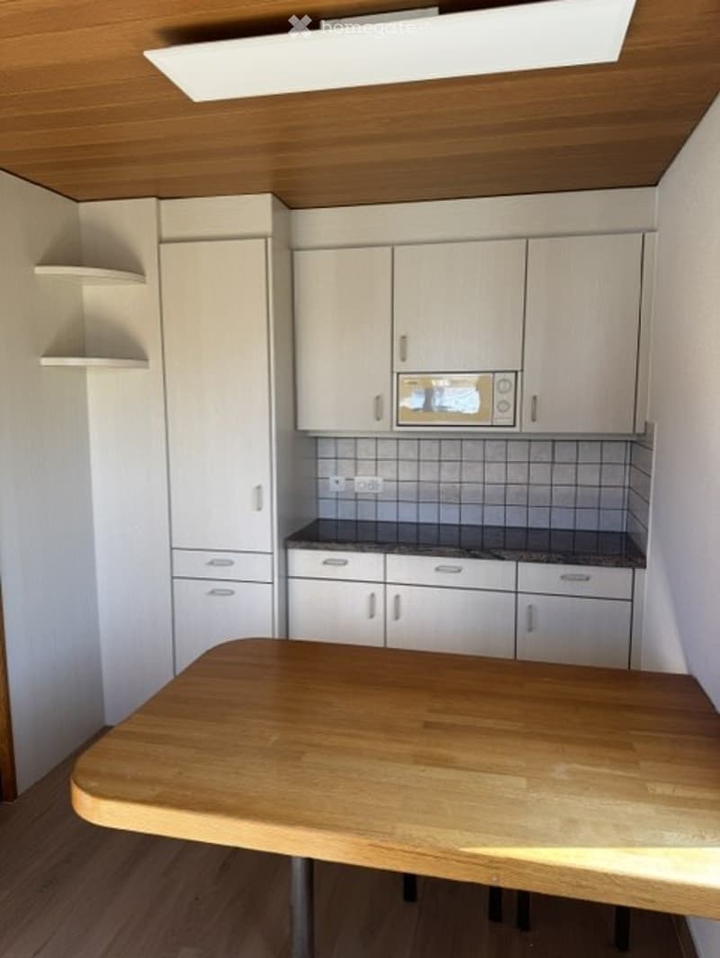 Modern kitchen with light-colored cabinets, a microwave, and a wooden dining table.