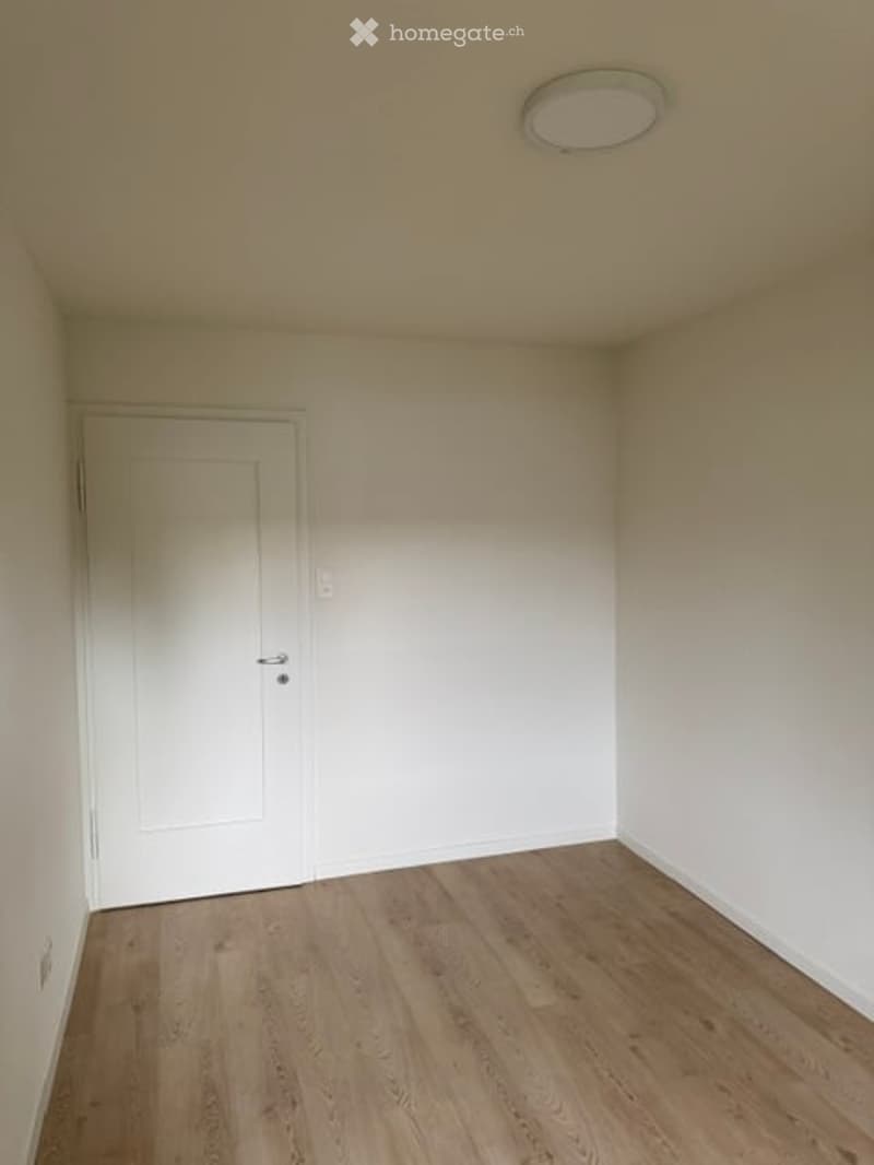Empty room with light wooden flooring, white walls, and a single white door.