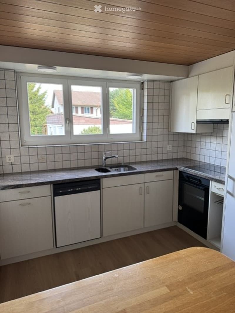 Modern kitchen with white cabinets, a wooden countertop, a sink with a faucet, a dishwasher, and an oven. The walls are tiled, and there is a large window offering a view of the outside.