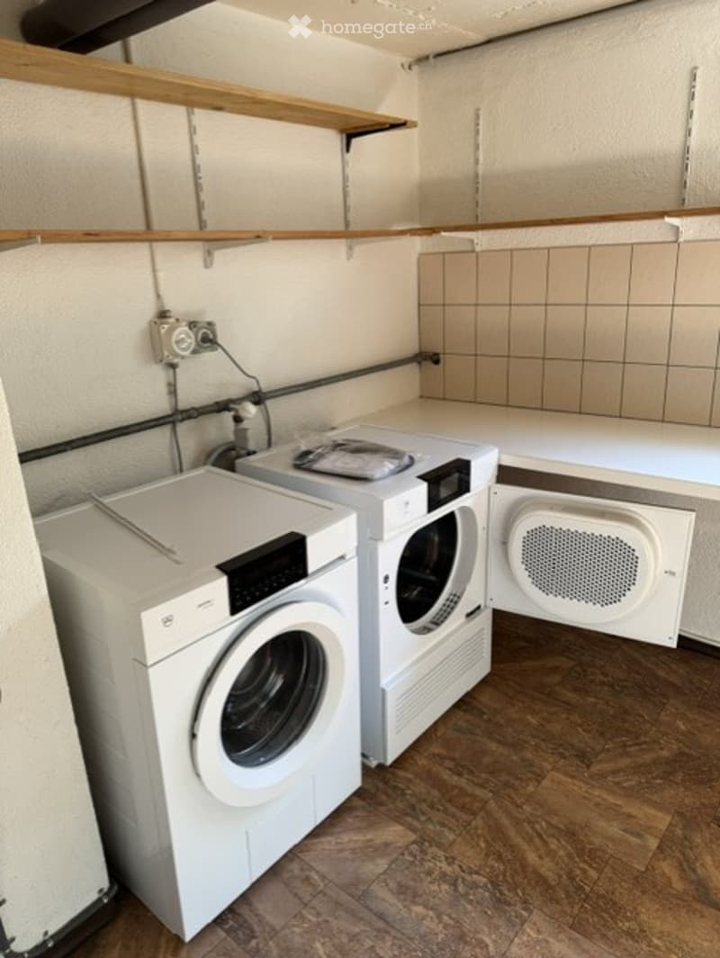 Laundry room with a washing machine, dryer, and wooden shelves.