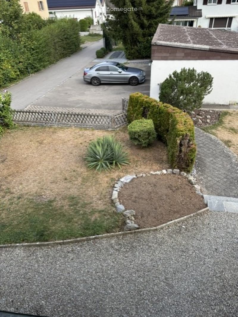 Front yard with gravel pathway, small garden bed, trimmed hedges, and a parked car in the driveway.