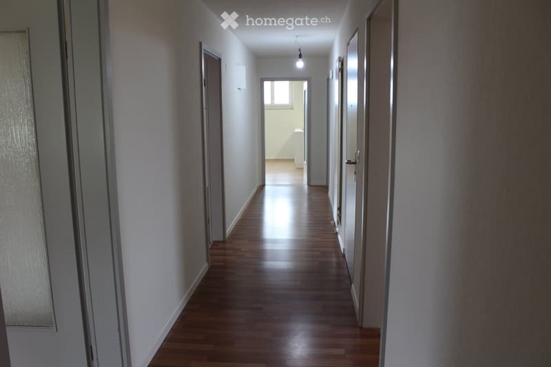 wooden floors, hallway leading to rooms, white walls, light hanging from ceiling