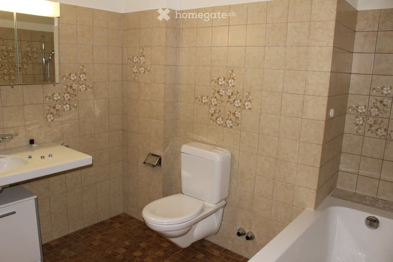 Beige tiled walls, beige tiled floor, white sink, white toilet, white bathtub, light fixture