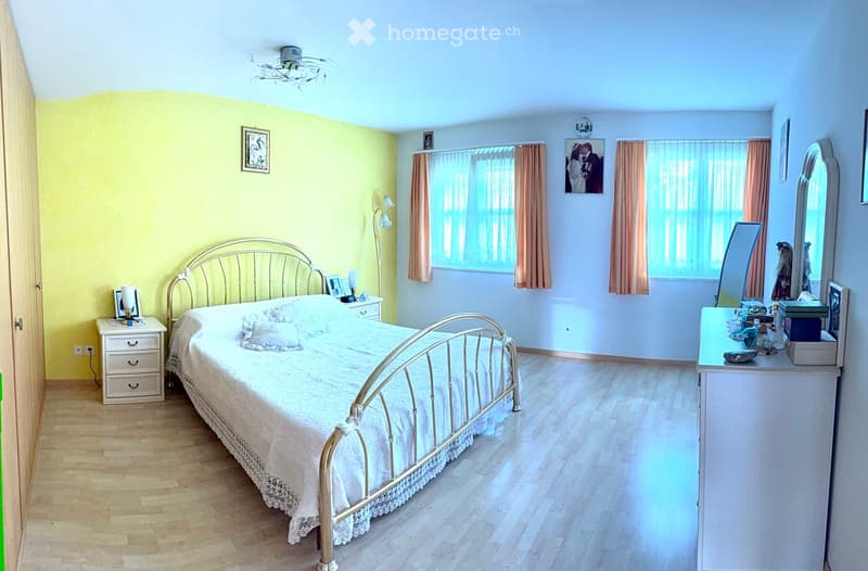 Bright bedroom with wooden flooring, a metal-framed bed with white bedding, a nightstand, a dresser with a mirror, and framed pictures on the walls.