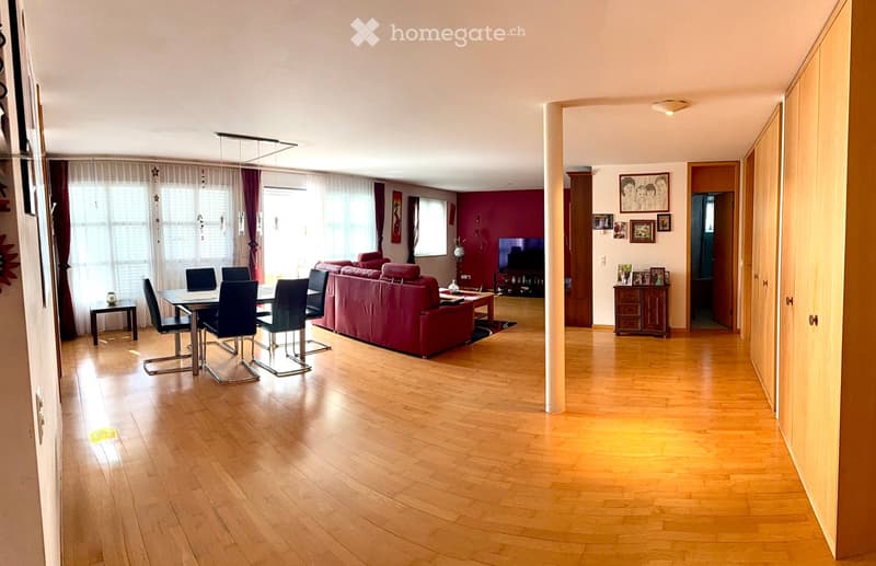 Open-plan living and dining area with wooden flooring, red sofa, dining table with chairs, television, and decorative wall art.