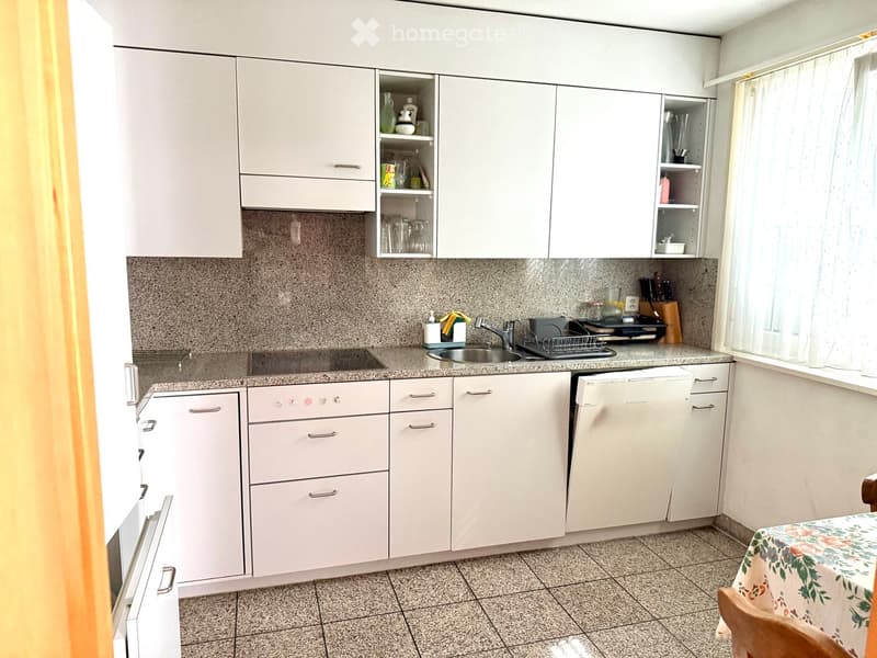 Modern kitchen with white cabinets, granite countertops, sink, dishwasher, and a small dining area with a table and chair.