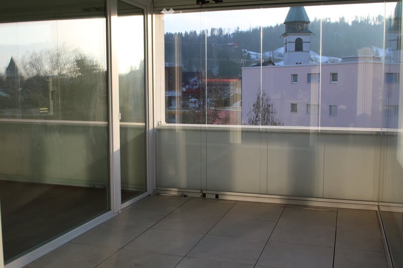 Modern balcony with large glass sliding doors, tiled floor, and scenic view of town and mountains.