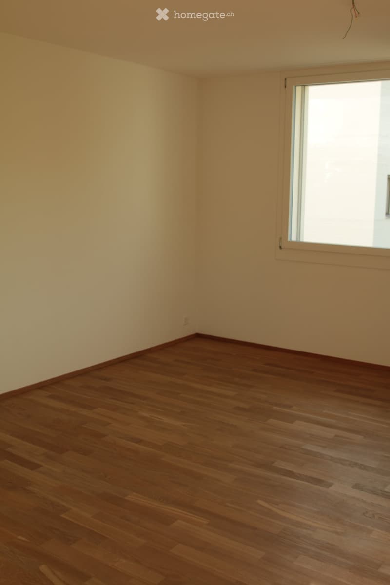 Empty room with wooden flooring and light-colored walls, featuring a large window on one side.