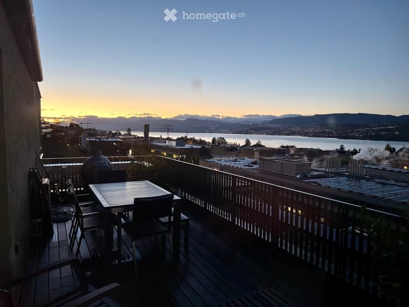 Balcony with a view of the city and water, featuring a table and chairs.