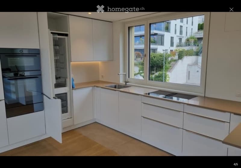 Modern kitchen with white cabinets, wooden countertops, stainless steel appliances, and large windows offering a view of the city.