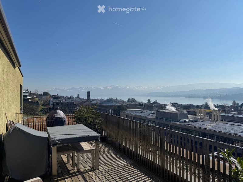 Balcony with wooden decking, covered furniture, and a scenic view of a cityscape, water, and distant mountains.