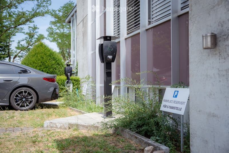 A modern building with a reserved parking spot for electric vehicles, featuring a charging station and a sign indicating the reserved space.