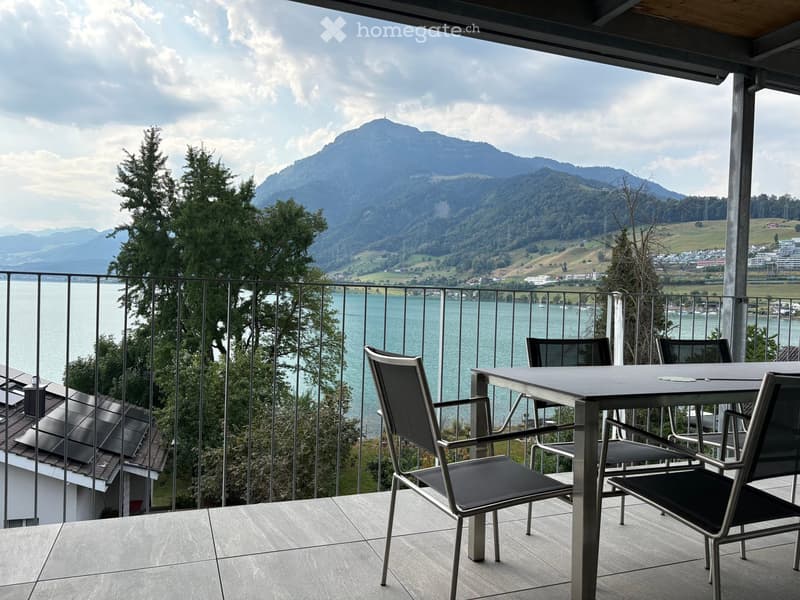 Balcony with a table and chairs, overlooking a lake and mountains.