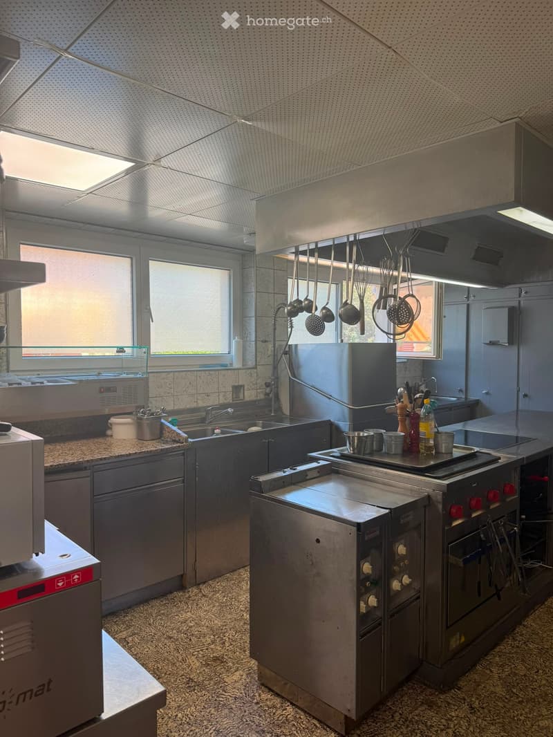 Modern commercial kitchen with stainless steel appliances, granite countertop, and hanging utensils.