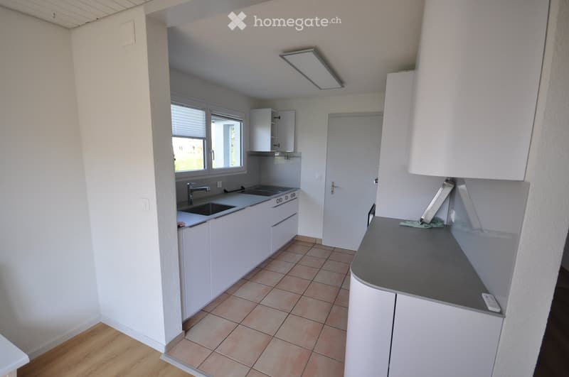 Modern kitchen with white cabinets, stainless steel sink, stove, and countertop. Features tiled flooring and a window with blinds.