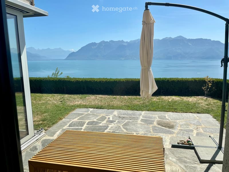 Outdoor patio with a wooden table, umbrella, and scenic mountain and lake view.