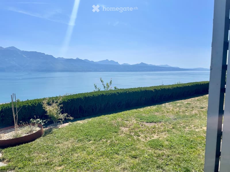 Garden with a well-maintained lawn, small plants, and a view of a lake and mountains in the background.