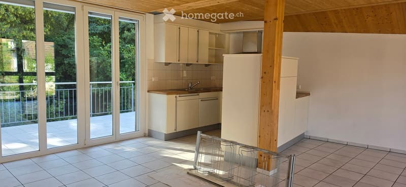 Bright kitchen with white cabinets, a sink, and a refrigerator. Large sliding glass doors lead to a balcony with a view of greenery.