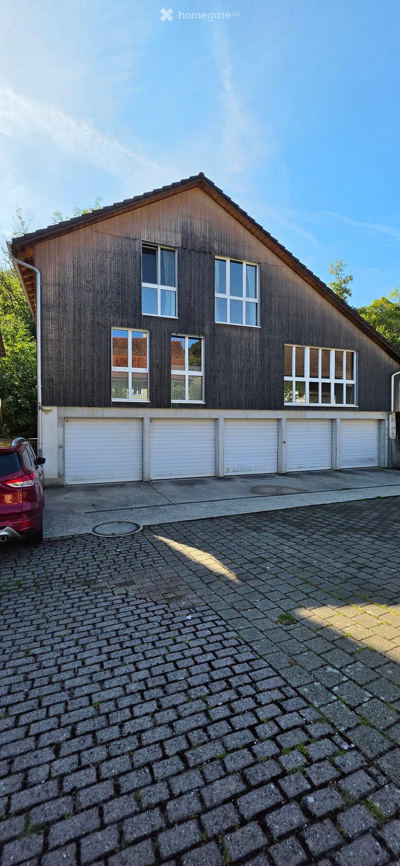 Two-story house with dark wooden siding, multiple windows, and a large garage section with multiple garage doors.